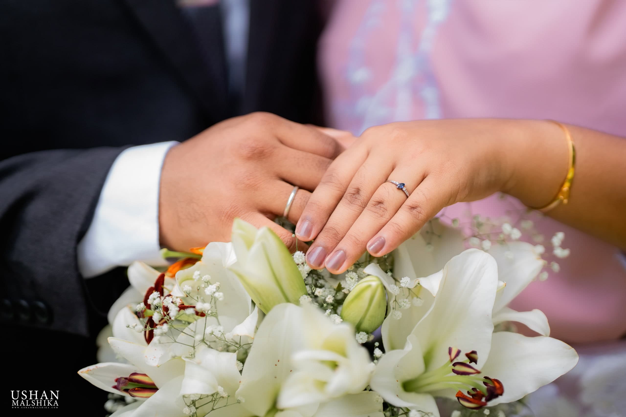 Hiruni and Ravindu showing their wedding rings over white lilies